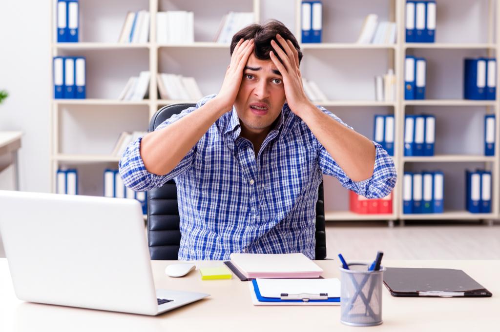A stressed man sitting at a desk in a modern office, looking overwhelmed and tired.